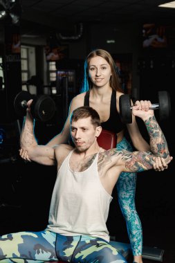 Aktif güzel fitness modeli kız erkek spor salonunda otururken dumbbells ile tren yardımcı olur.