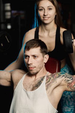 Aktif güzel fitness modeli kız erkek spor salonunda otururken dumbbells ile tren yardımcı olur.