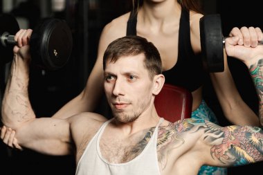 Aktif güzel fitness modeli kız erkek spor salonunda otururken dumbbells ile tren yardımcı olur.