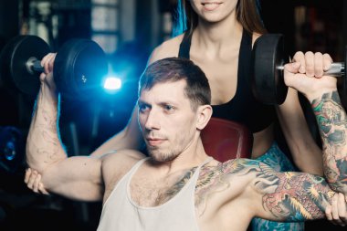 Aktif güzel fitness modeli kız erkek spor salonunda otururken dumbbells ile tren yardımcı olur.