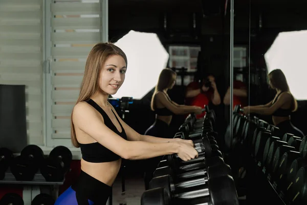 Activa hermosa chica modelo de fitness toma pesas de bastidores para hacer ejercicio en el gimnasio . —  Fotos de Stock