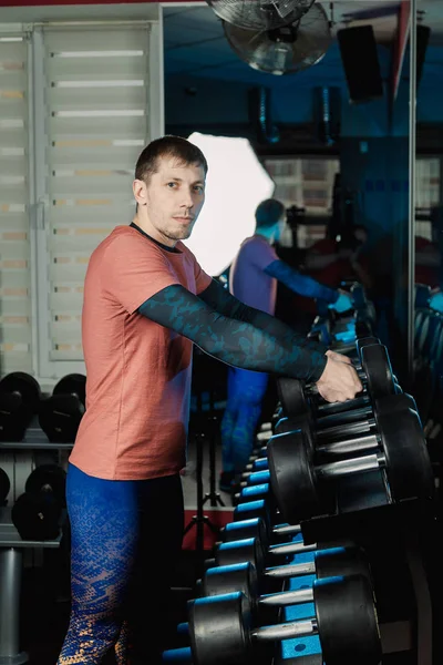 Przystojny lekkoatletycznego mężczyzna bierze hantle od Stojaki do dalszego treningu w siłowni. — Zdjęcie stockowe