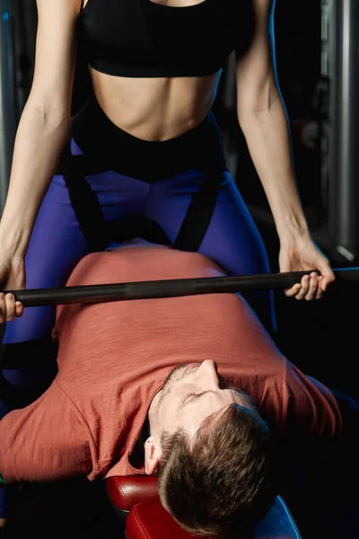 Female trainer helping guy to train in the gym Bar Bench Press.