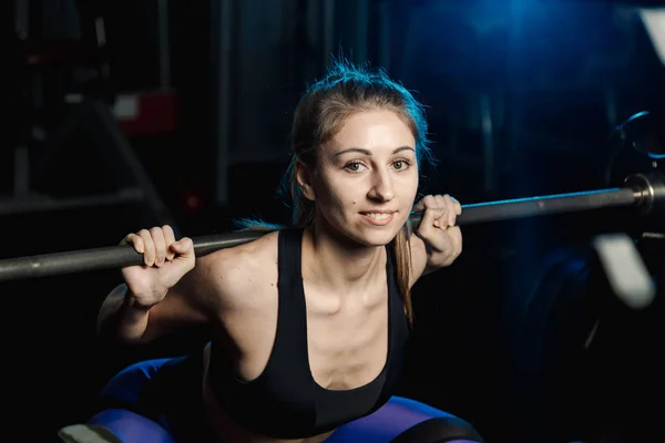 Active beautiful fitness model girl crouches with a barbell on the shoulders in the gym. — Stock Photo, Image