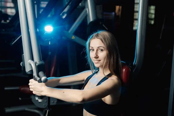 Active beautiful fitness model girl trains pectoral muscles on a simulator in the gym. — Stock Photo, Image