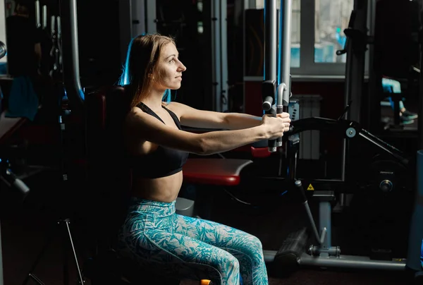 Activa hermosa chica modelo fitness entrena los músculos pectorales en un simulador en el gimnasio . — Foto de Stock