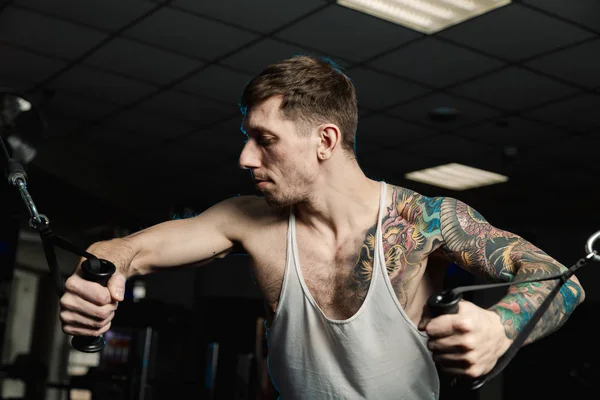 Göğüs kasları bir blok simülatör spor salonunda yakışıklı atletik erkek trenler.