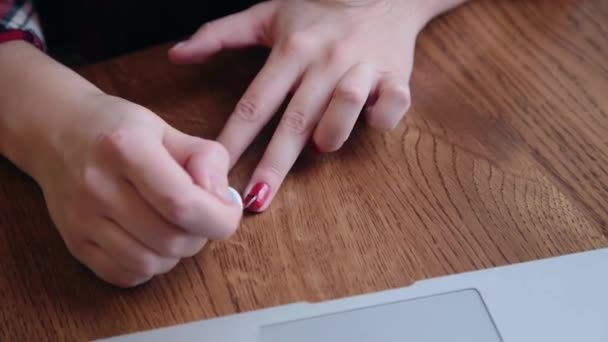 Eine schöne Geschäftsfrau sitzt an einem Tisch mit einem Laptop in einem Café und lackiert ihre Nägel. — Stockvideo