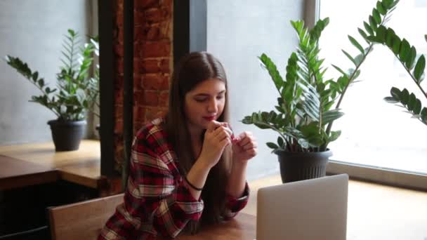 Μια όμορφη επιχειρηματίας κάθεται σε ένα τραπέζι με ένα φορητό υπολογιστή σε μια καφετέρια και βάφει τα νύχια της. — Αρχείο Βίντεο