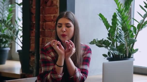 Una hermosa mujer de negocios se sienta en una mesa con un portátil en un café y se pinta las uñas . — Vídeos de Stock