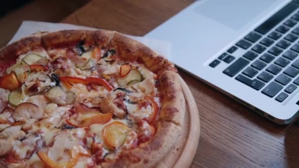 Pizza en una mesa de madera junto a un portátil . — Vídeo de stock