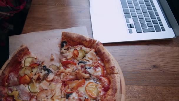 Πίτσα σε ένα ξύλινο τραπέζι δίπλα σε ένα φορητό υπολογιστή. — Αρχείο Βίντεο