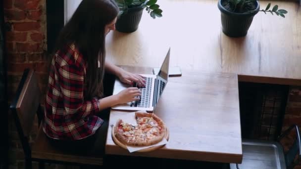 Schöne attraktive Geschäftsfrau arbeitet hinter einem Laptop in einem Café, Pizza auf dem Tisch. — Stockvideo