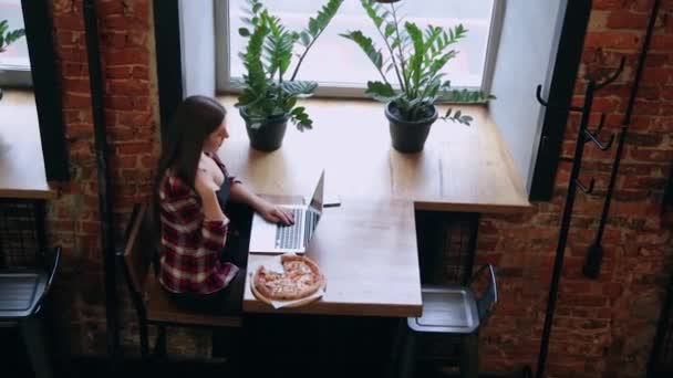 Gyönyörű, vonzó üzleti nő dolgozik mögött egy laptop a kávézóban, a pizza, az asztalon. — Stock videók