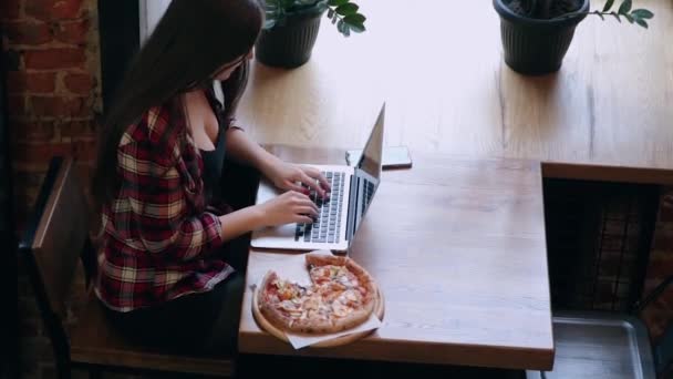 Gyönyörű, vonzó üzleti nő dolgozik mögött egy laptop a kávézóban, a pizza, az asztalon. — Stock videók