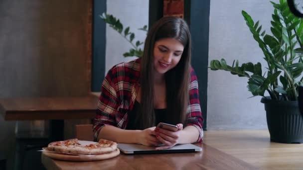 Schöne attraktive Geschäftsfrau, die mit Telefon und Laptop an einem Tisch in einem Café sitzt. Pizza auf dem Tisch. — Stockvideo