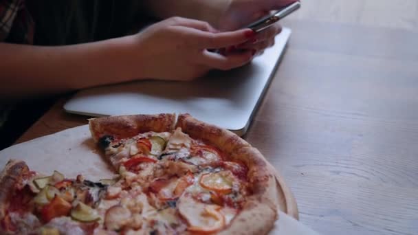 Mooie aantrekkelijke zakenvrouw zittend met een telefoon en een laptop aan een tafel in een café. Pizza op tafel. — Stockvideo