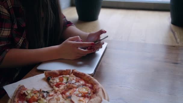 Schöne attraktive Geschäftsfrau, die mit Telefon und Laptop an einem Tisch in einem Café sitzt. Pizza auf dem Tisch. — Stockvideo