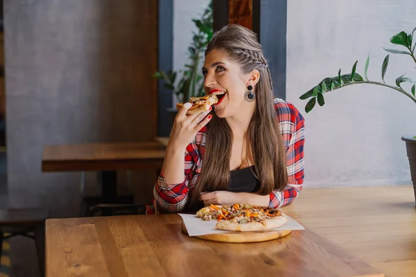 Hermosa y sexy chica sentada junto a la ventana en un café y comiendo pizza . — Foto de Stock