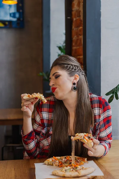 Hermosa y sexy chica sentada junto a la ventana en un café y comiendo pizza . — Foto de Stock