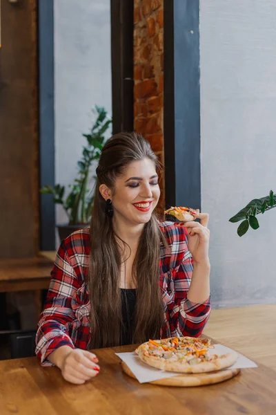 Hermosa y sexy chica sentada junto a la ventana en un café y comiendo pizza . — Foto de Stock