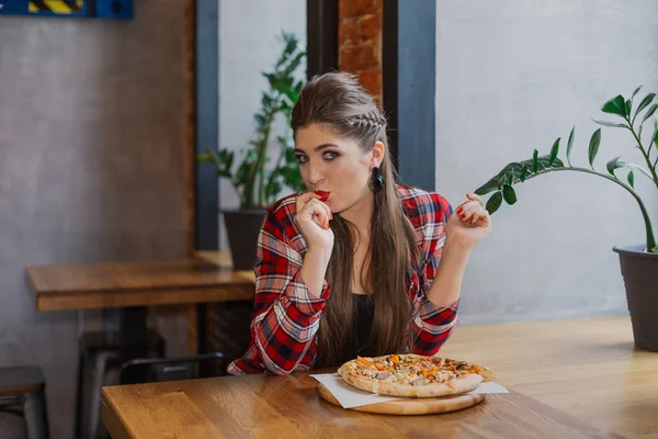 Hermosa y sexy chica sentada junto a la ventana en un café y comiendo pizza . — Foto de Stock