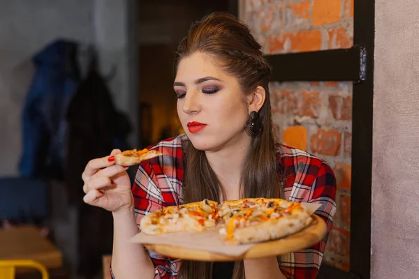 Menina bonita e sexy sentada à janela em um café e comer pizza . — Fotografia de Stock