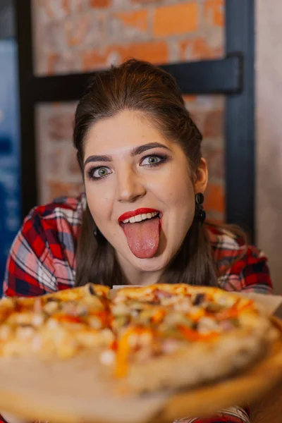 Beautiful and sexy girl sitting by the window in a cafe and eating pizza. — Stock Photo, Image