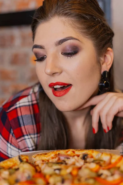 Красива і сексуальна дівчина сидить біля вікна в кафе і їсть піцу . — стокове фото
