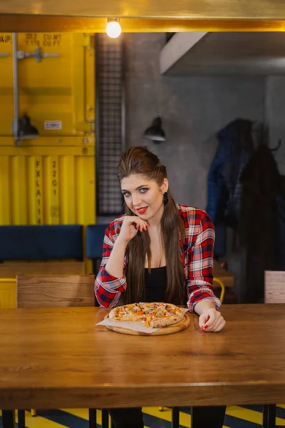 Belle et sexy fille assise à une table avec une pizza dans un café . — Photo