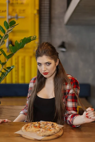 Mooi en sexy meisje zitten aan een tafel met een pizza in een café. — Stockfoto