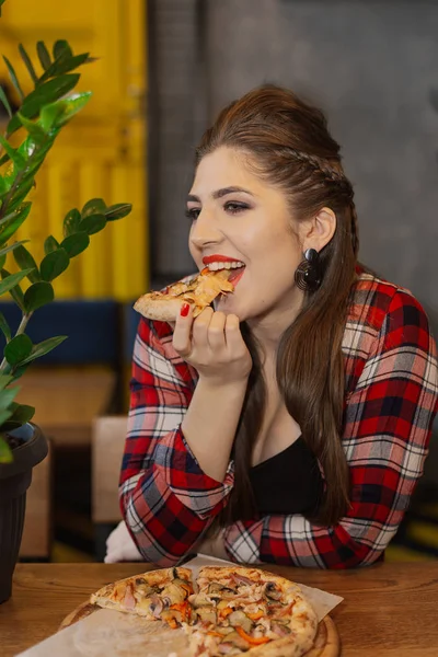 Hermosa y sexy chica sentada en una mesa con una pizza en un café . — Foto de Stock