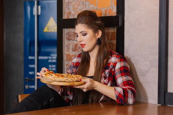 Menina bonita e sexy sentada à janela em um café e comer pizza . — Fotografia de Stock