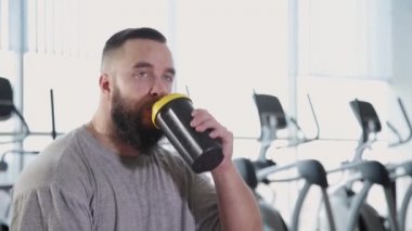 Yakışıklı atletik bir protein shaker açar ve spor salonunda içecekler.
