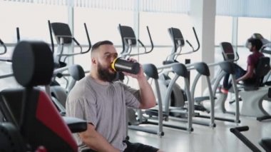 Yakışıklı atletik bir protein shaker açar ve spor salonunda içecekler.