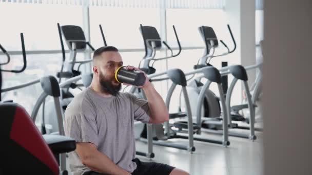 Atletický muž otevře bílkovin třepačce a pije v tělocvičně. — Stock video