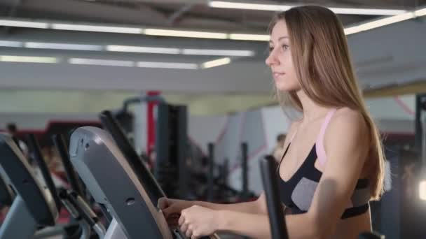Schöne athletische junge Mädchen trainiert auf einem Crosstrainer in der Turnhalle. — Stockvideo