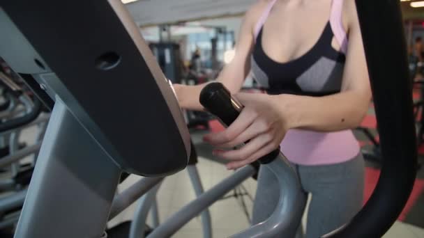 Beautiful athletic young girl trains on an elliptical trainer at the gym. — Stock Video