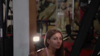 Spor salonunda omuzlarında güzel atletik genç kız crouches.