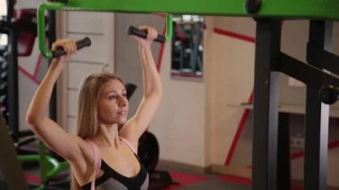 Güzel atletik genç kız göğüs simülatör spor salonunda bir çekme gerçekleştirir.