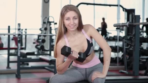 Hermosa atlética joven entrena pesas bíceps en el gimnasio . — Vídeo de stock