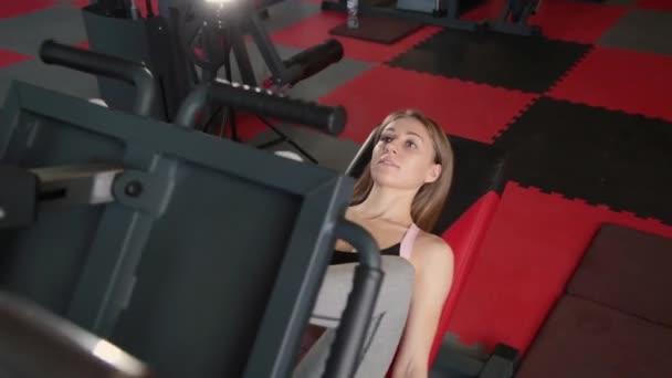 La chica está en el gimnasio haciendo la máquina de prensa de piernas . — Vídeos de Stock