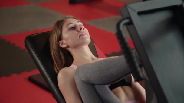 La chica está en el gimnasio haciendo la máquina de prensa de piernas . — Vídeo de stock