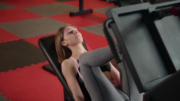 Η κοπέλα είναι στο γυμναστήριο κάνει το πόδι μηχανή τύπου. — Αρχείο Βίντεο