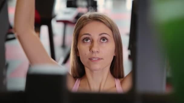 Bela menina atlética executa uma tração no simulador de peito no ginásio . — Vídeo de Stock