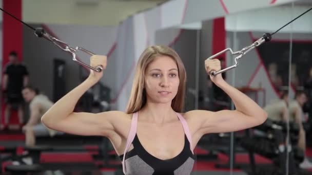 Hermosa chica atlética entrena bíceps en un simulador de bloque en el gimnasio . — Vídeos de Stock