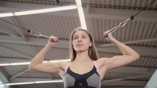 Mooi sportieve jonge meisje traint biceps op een blok simulator simulator in de sportschool. — Stockvideo