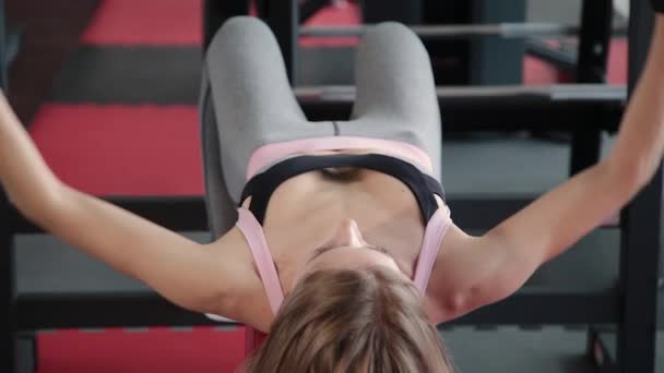Beautiful athletic young girl dumbbell exercises the pectoral muscles in the gym. — Stock Video