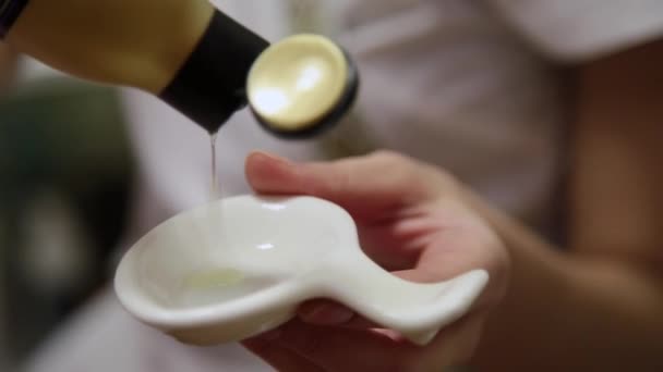Массажист заливает масло для массажа в деревянную миску. Подготовка к массажу в роскошном спа-салоне — стоковое видео
