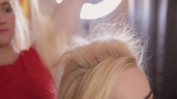 Eine junge Frau sitzt im Friseursessel, ein Friseur frisiert. eine junge blonde Frau kam in den Schönheitssalon, um sich eine stylische Frisur zu machen. — Stockvideo